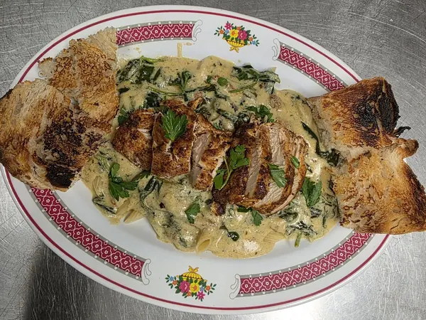 Sliced blackened chicken over penne in a creamy spinach sauce with toasted bread on the side.
