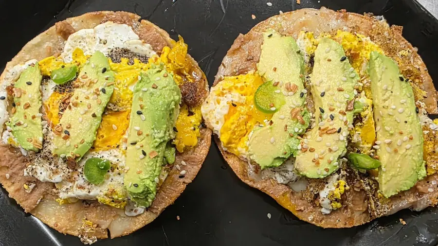 Two crisp tostadas topped with refried beans, fried egg, sliced avocado, jalapeño and everything-bagel seasoning.