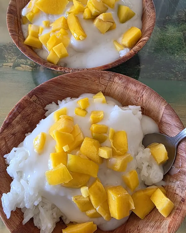 Two wooden bowls of sticky rice with coconut cream and fresh diced mango.