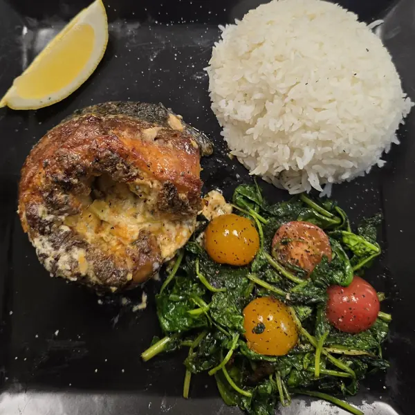 A stuffed salmon fillet plated with jasmine rice, sautéed spinach, cherry tomatoes and a lemon wedge.