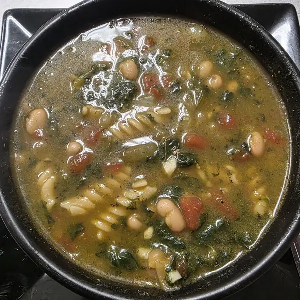 A bowl of brothy soup with white beans, spinach, tomato and spiral pasta.